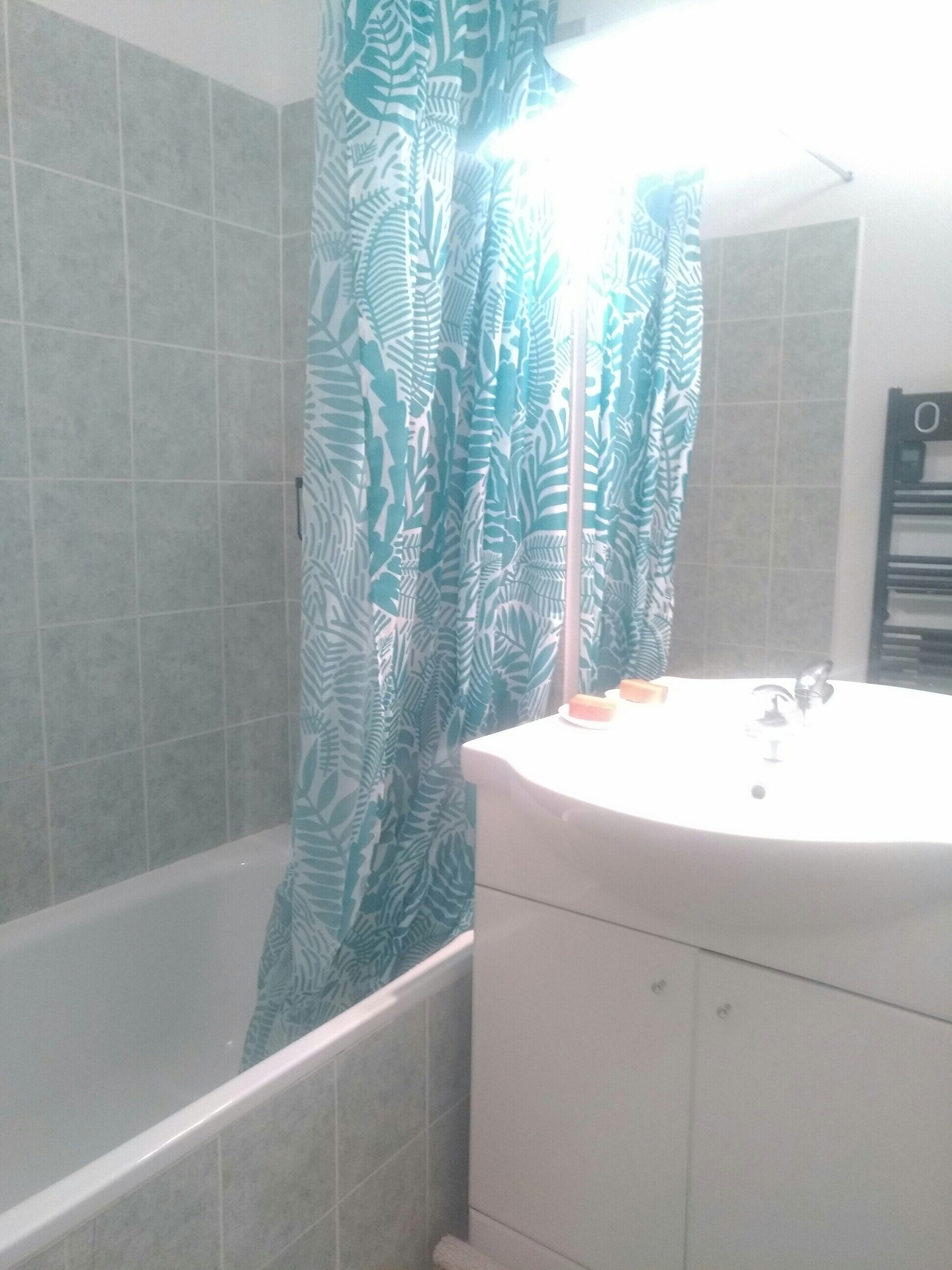 A bathroom with a bathtub, a sink, and a shower curtain with a leaf pattern.