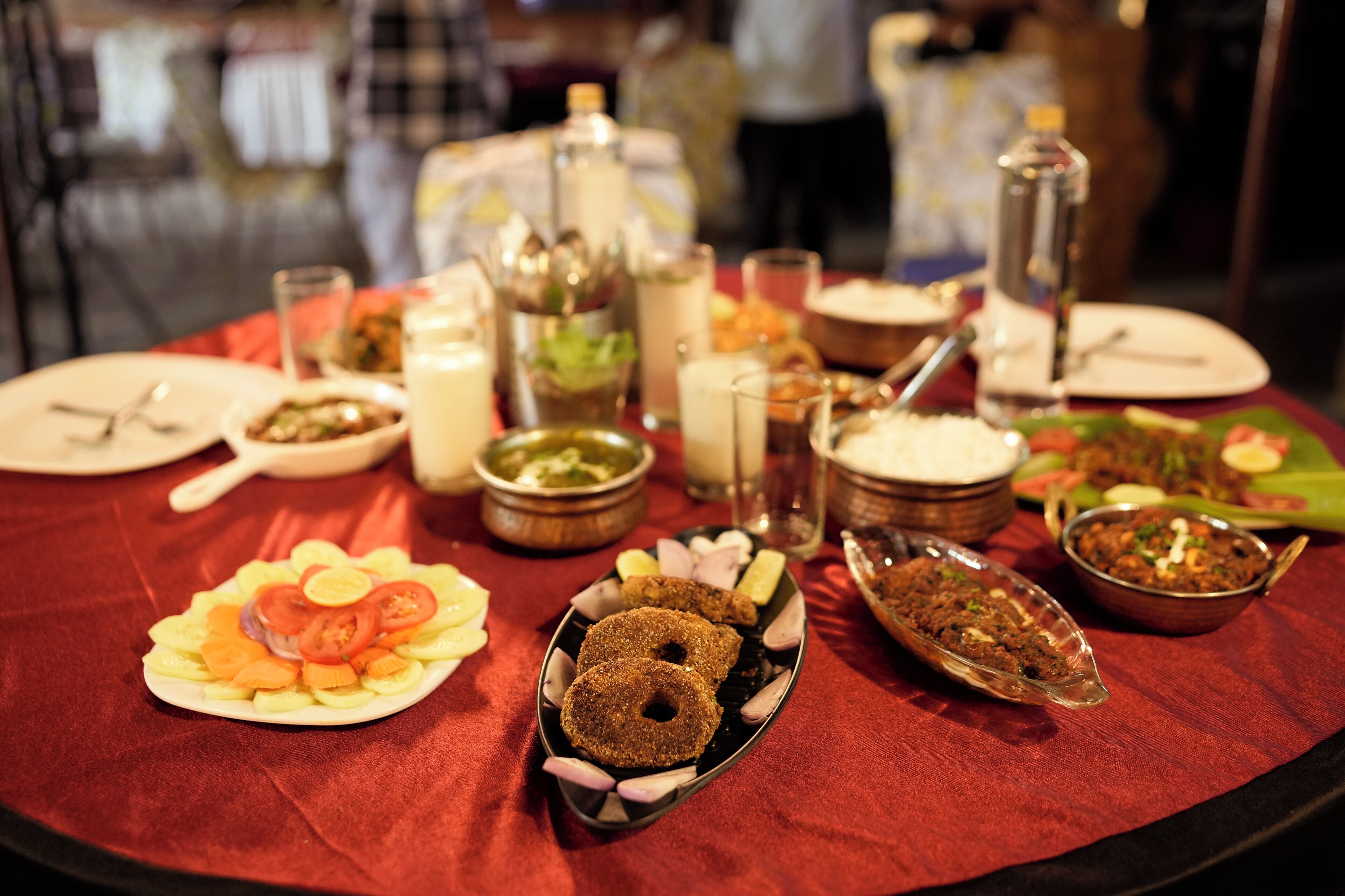 A table set with various dishes and drinks, including a plate of sliced vegetables, a bowl of salad, and a glass of water.