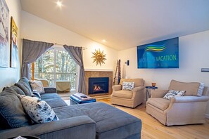 A modern living room with a fireplace, comfortable seating, and a large TV screen displaying 'Michael's Vacation Rentals'. - 2BD Ranch Condo - Walk to FREE Elkhorn Resort Amenities (Sun Valley)