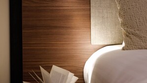 A neatly made bed with a headboard, a bedside table with a book, and a wall-mounted light.
