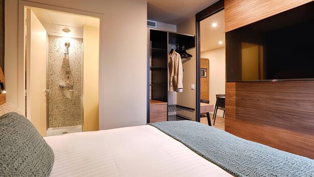 A modern hotel room with a bed, a shower, a wardrobe, and a desk.