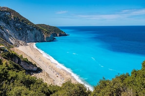 Une plage côtière aux eaux bleues et limpides, bordée d’un rivage sablonneux et de falaises rocheuses.