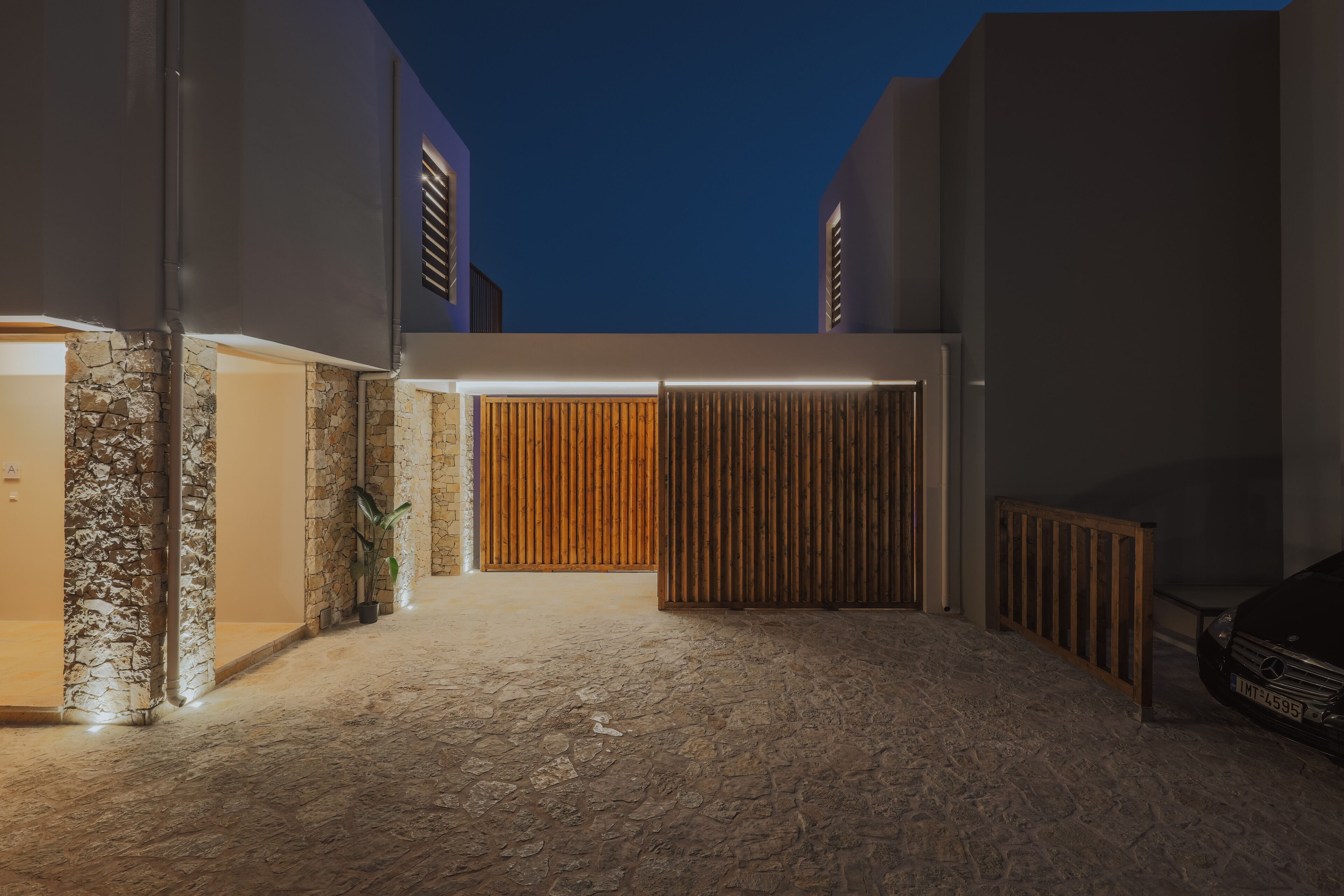 A modern building with a stone facade, a wooden gate, and a car parked outside.