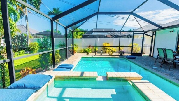 Una piscina con un recinto in vetro, circondata da sdraio e vista su un giardino.
