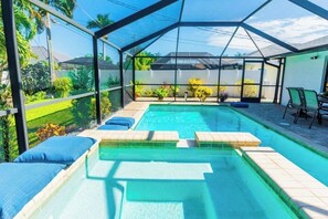 A swimming pool with a glass enclosure, surrounded by lounge chairs and a garden view. - 733 Sunset Hideaway | Pool & Spa (Naples)