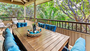 Eine Terrasse im Freien mit einem Holztisch, gedecktem Esstisch, blauen Sitzkissen und Blick auf üppige tropische Vegetation.