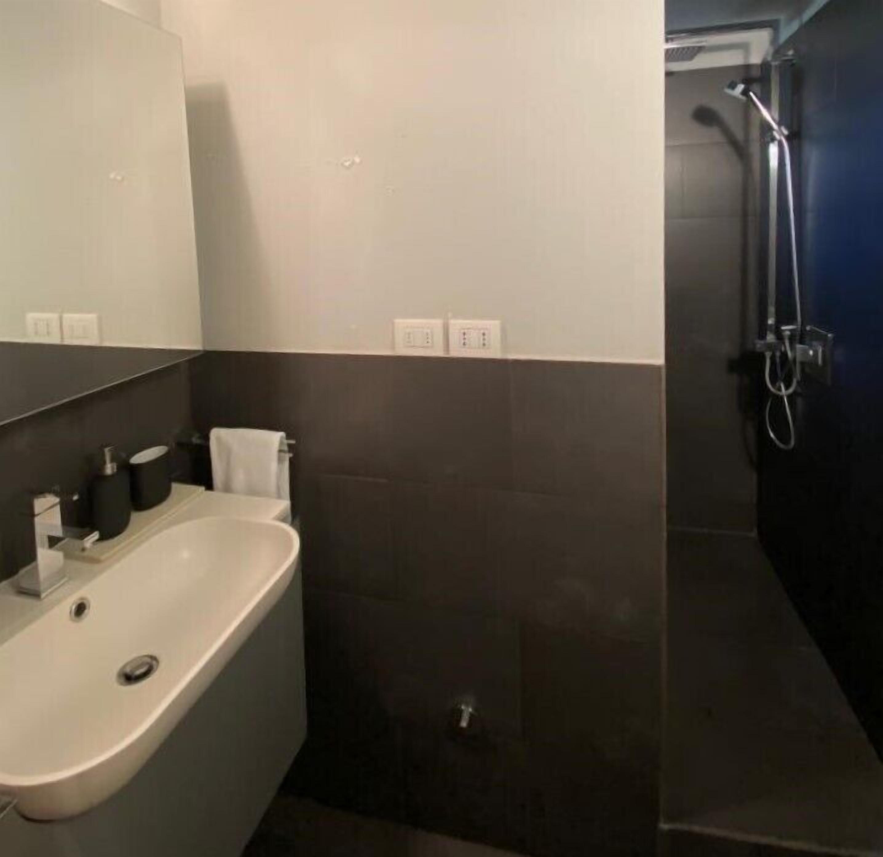 A modern bathroom with a white sink, dark tiles, a mirror, and a shower area.