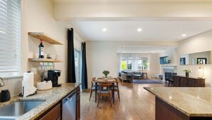 A modern kitchen with granite countertops, wooden cabinets, and a central island. There is a dining area with a table and chairs, and a living room with a sofa and coffee table. - 3BR Hillsboro Home · Sleeps 6 · Intel · Pets OK (Hillsboro)