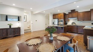 A modern kitchen with wooden cabinets, a central island, and a dining area with a table and chairs. - 3BR Hillsboro Home · Sleeps 6 · Intel · Pets OK (Hillsboro)
