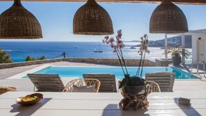 A poolside view with wicker lamps, a table with a bowl, and a view of the sea and boats. - My Rental Homes - Villa Sonia with pool, Jacuzzi bathtub, sea view (Platis Gialos)
