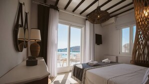 A bedroom with a bed, a desk, a lamp, a large window with a view of the sea, and a ceiling fan. - My Rental Homes - Villa Sonia with pool, Jacuzzi bathtub, sea view (Platis Gialos)