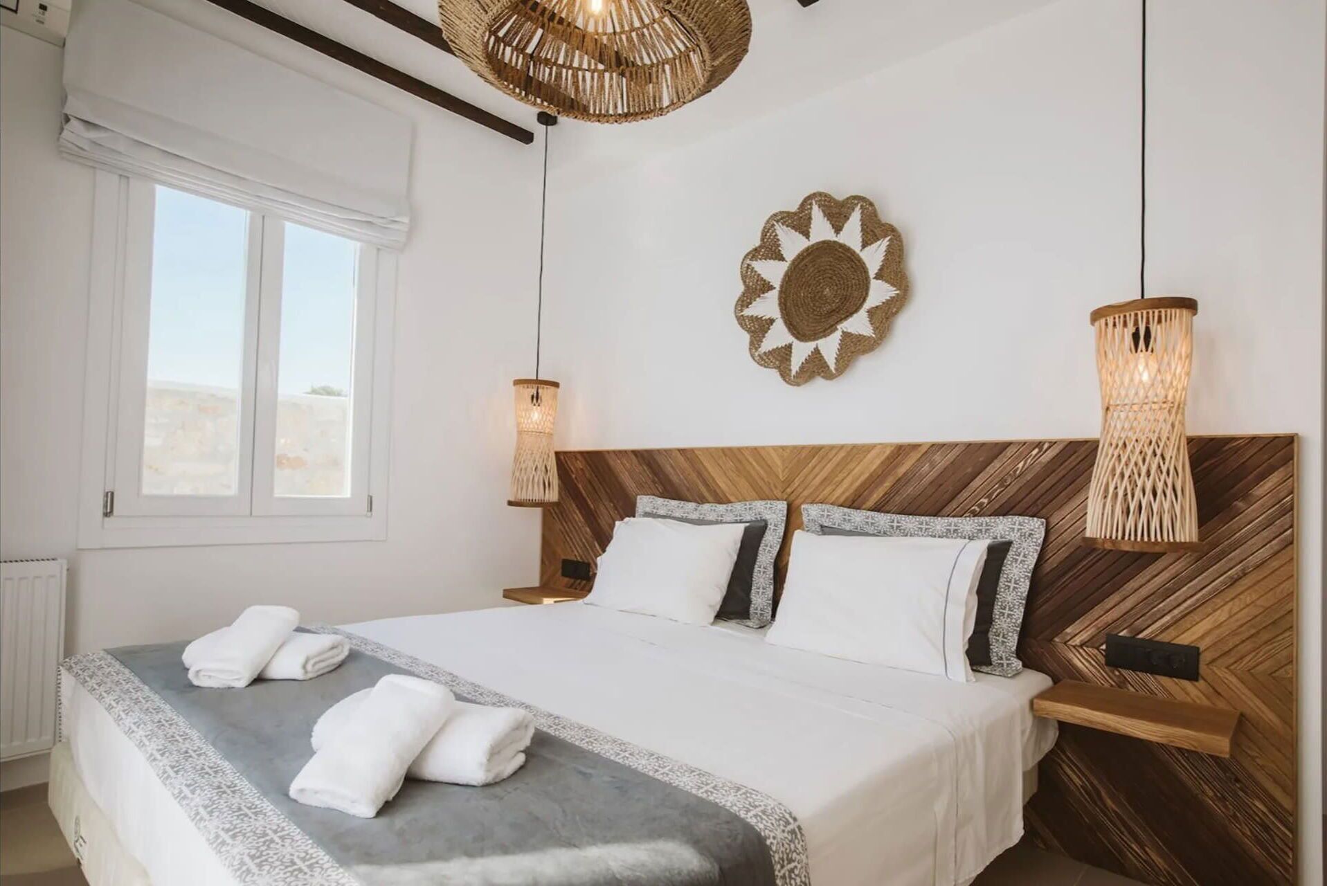 A neatly made bed with white linens and two towels, a wooden headboard, and a decorative wall piece.