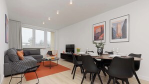 Una sala moderna con un sofá gris, una silla de estructura negra, una mesa de comedor con sillas negras y un televisor sobre un mueble.