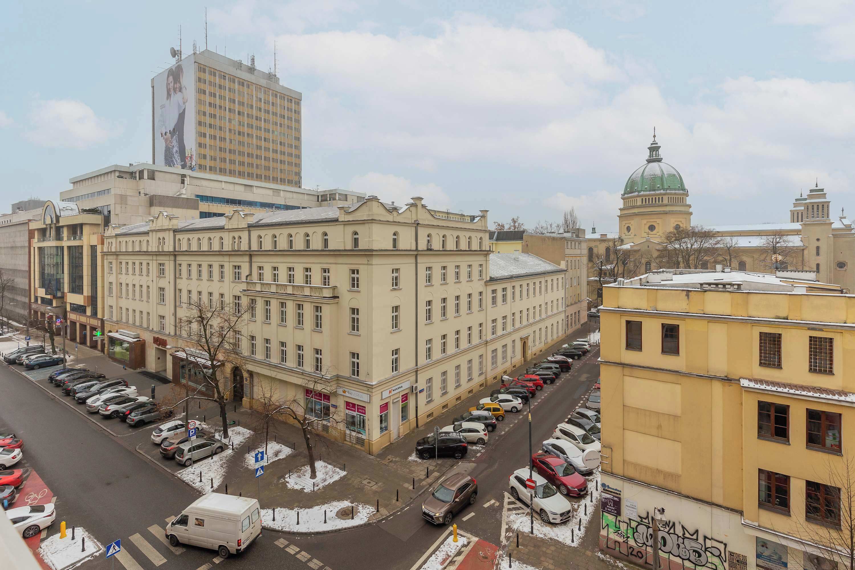 A multi-story building with a classical architectural style, featuring a central courtyard and a dome structure in the background.
