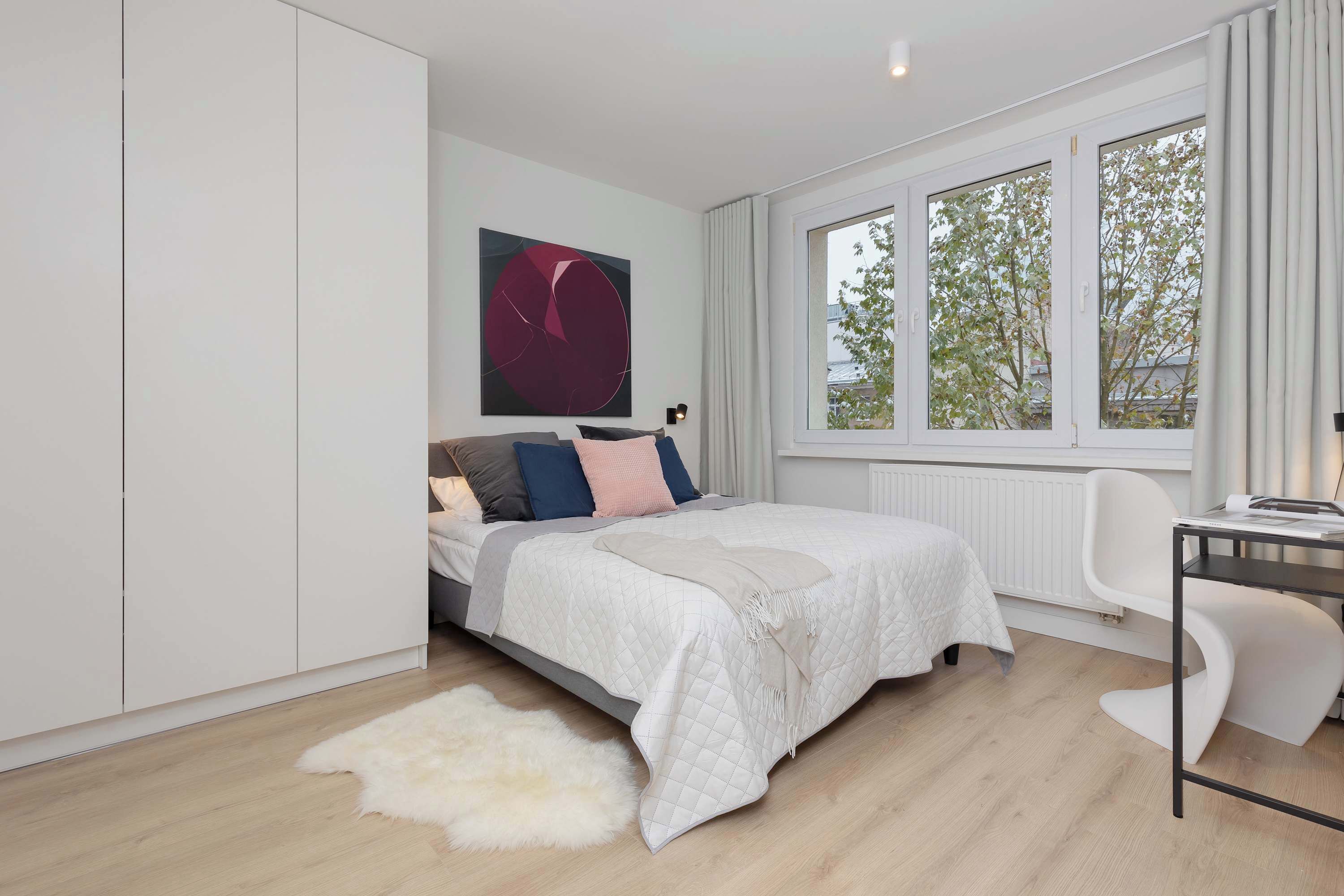 Un dormitorio moderno con cama, escritorio y un ventanal grande.