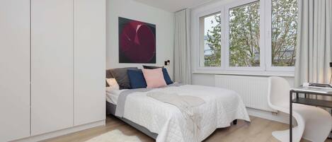 Un dormitorio moderno con cama, escritorio y un ventanal grande.