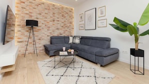 A modern living room with a grey sectional sofa, a black floor lamp, a round coffee table, and a large potted plant.