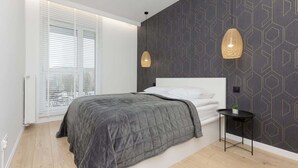 A modern bedroom with a large bed, a small bedside table, and a geometric-patterned wall.