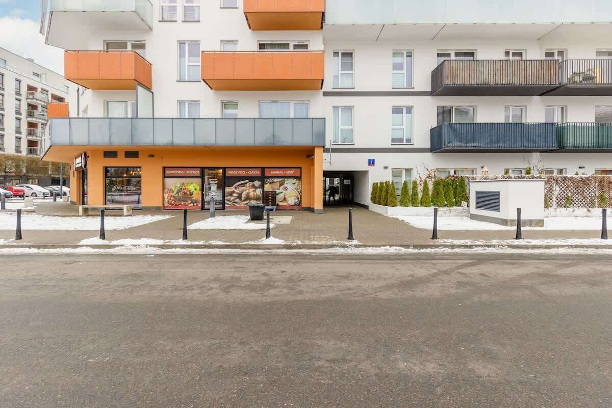 A multi-story building with balconies, a ground-level entrance, and a visible restaurant with outdoor seating.