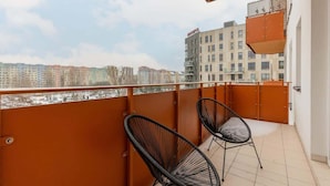A balcony with two black wicker chairs, a wooden table, and a view of a cityscape with buildings in the background.