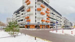A multi-story residential building with balconies, a storefront, and a parking area.