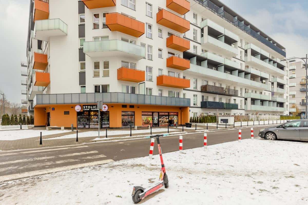 A multi-story residential building with balconies, a storefront with a sign, and a parked scooter.