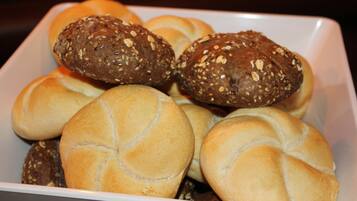 Een schaal met verschillende soorten broodjes, waaronder sesam en zaden, op een wit bord.