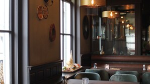 Un interior de restaurante con mesas de madera, sillas tapizadas en verde y lámparas colgantes.