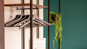 A clothing rack with hangers and a potted plant against a teal wall.