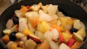 A bowl of mixed fruit salad with various fruits and a black spoon.