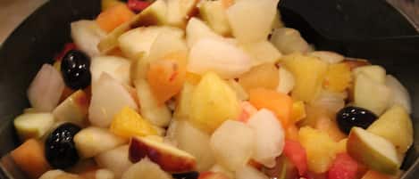 Un tazón de ensalada de frutas mixtas con diversas frutas y una cuchara negra.
