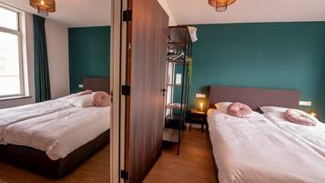 Une chambre d’hôtel avec deux lits, une armoire, une étagère avec des vêtements suspendus et une fenêtre avec des rideaux.