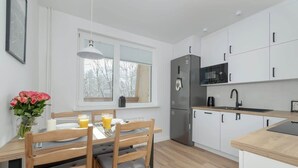 A modern kitchen with white cabinets, a stainless steel refrigerator, a microwave, and a sink. There is a dining table with chairs and a vase of flowers. - Apartment with a View of the Tatra Mountains | Balcony | 600 m to the Center (Zakopane)