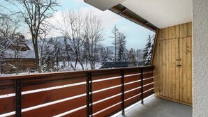 A balcony with a wooden railing overlooking a snowy landscape with trees and a building in the background. - Apartment with a View of the Tatra Mountains | Balcony | 600 m to the Center (Zakopane)