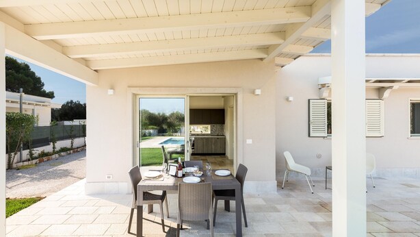 Eine Außenpatio mit Tisch und Stühlen, einem überdachten Bereich und Blick auf Pool und Grünflächen.