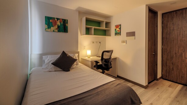 A bedroom with a bed, a desk, a chair, and a door. - DAS HAUS  (Bogotá)