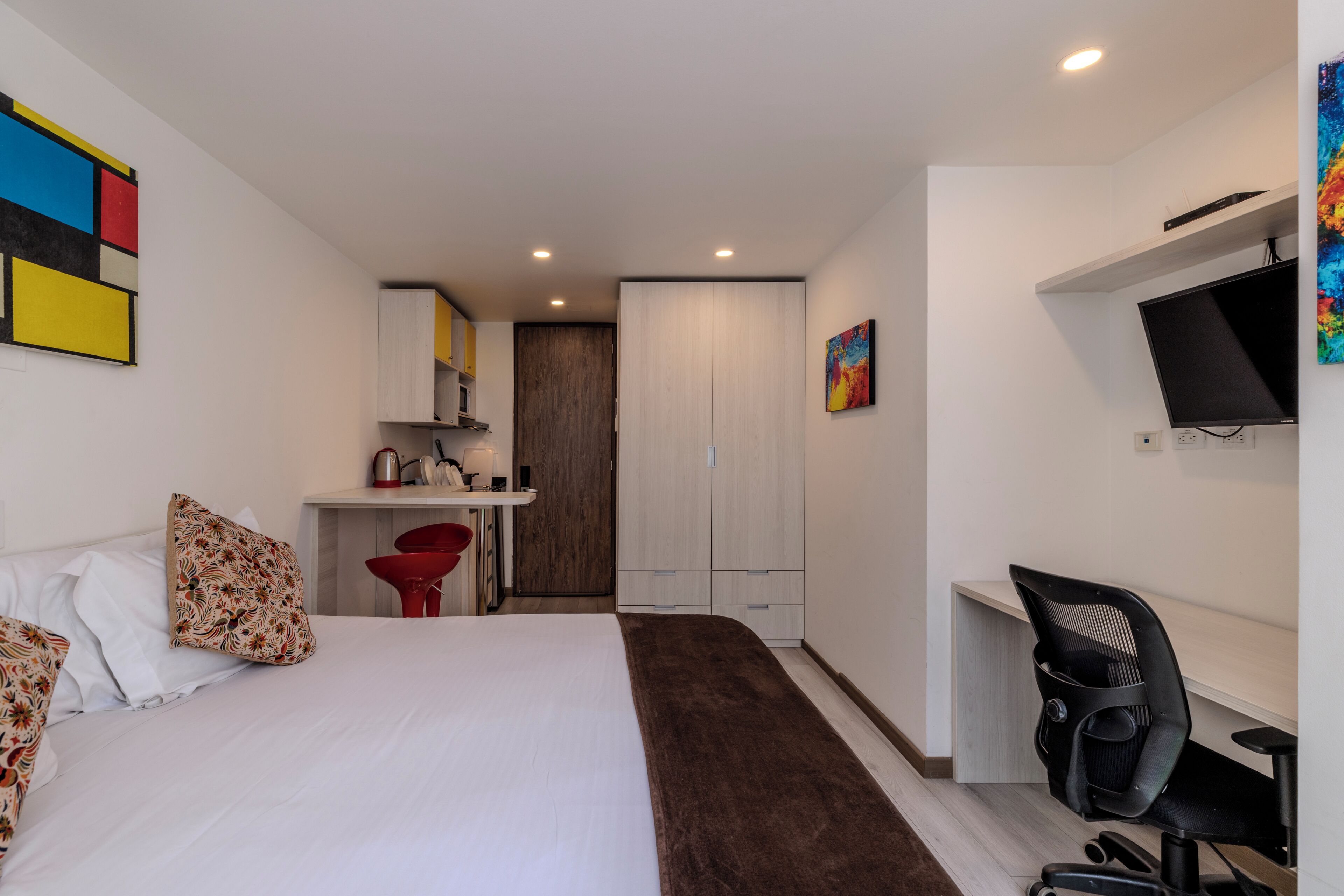 A compact hotel room with a bed, a desk, a chair, a TV, and a wardrobe.
