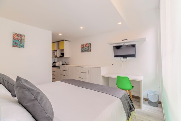 A hotel room with a bed, a desk, a television, and a kitchenette.