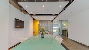 A conference room with a glass table, white chairs, a potted plant, and a yellow accent wall. - DAS HAUS  (Bogotá)