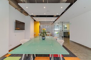 Ein Konferenzraum mit Glastisch, weißen Stühlen, einem Blumentopf und einer gelben Akzentwand.
