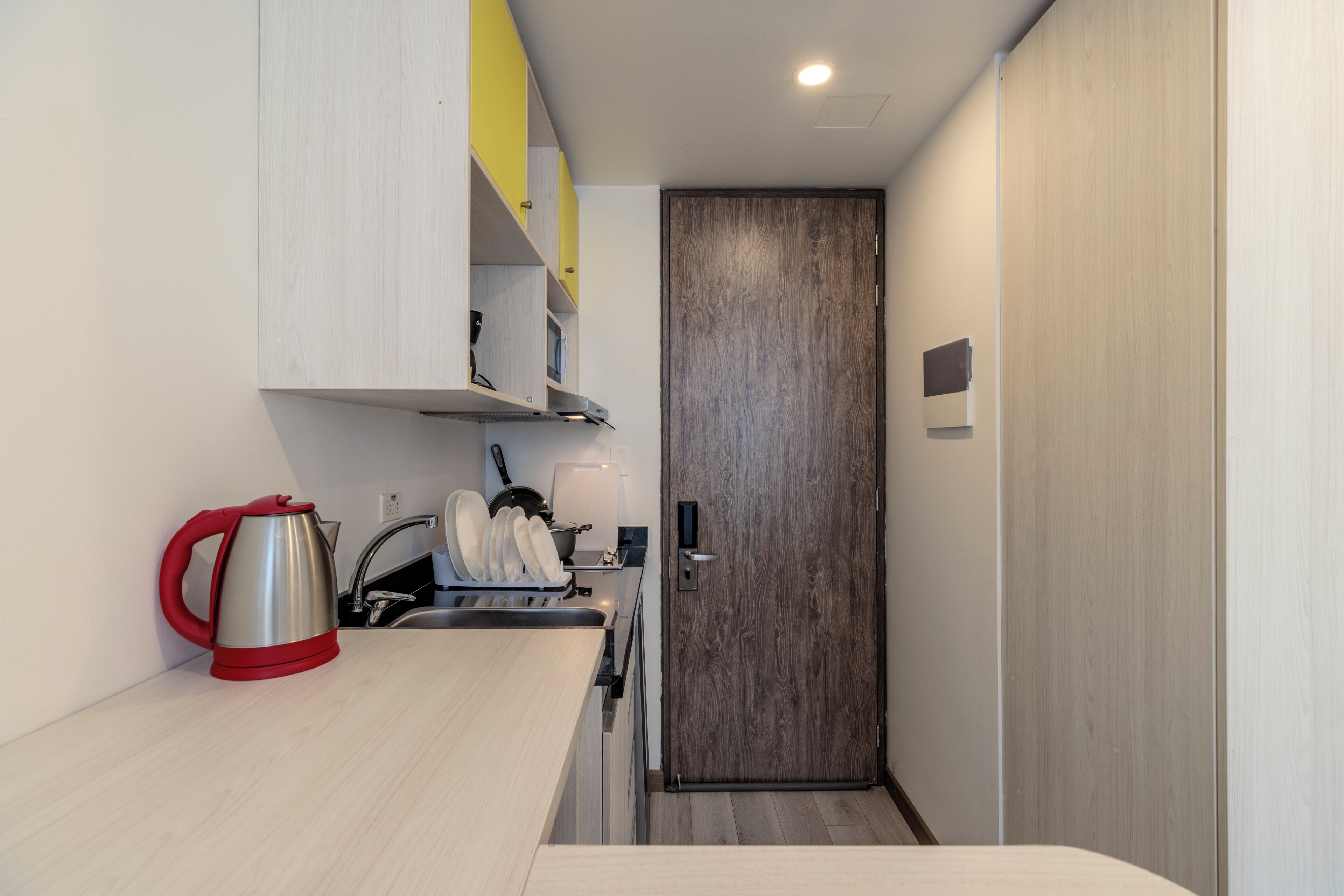 Una kitchenette compacta con un lavabo, una tetera y un escurreplatos.