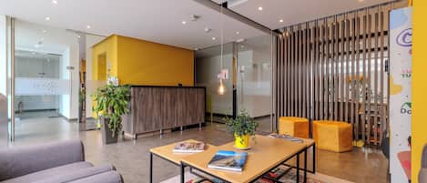 A modern reception area with a wooden reception desk, a colorful rug, and a seating area with two ottomans.