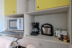 Une petite cuisine équipée d’un four à micro-ondes, d’une machine à café et d’une étagère avec des tasses et des bocaux.