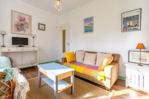 Ein Wohnzimmer mit einer Couch, einem Fernseher, einem Tisch und einem gerahmten Bild an der Wand.