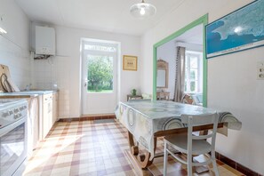 Une cuisine avec un sol carrelé, une table à manger avec des chaises, une fenêtre donnant sur un espace verdoyant et un miroir fixé au mur.