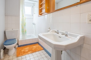 Une salle de bain équipée de toilettes, d’un lavabo, d’une douche et d’une étagère en bois au-dessus du lavabo.