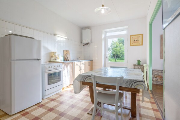 A kitchen with a refrigerator, oven, and dining table with chairs.