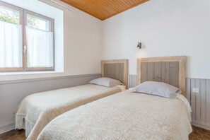 Een kamer met twee bedden, houten hoofdborden, een raam met gordijnen en een lamp aan de muur.