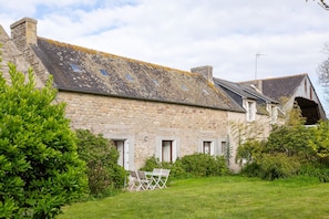 A stone building with a sloped roof, a small lawn, and a white folding table.