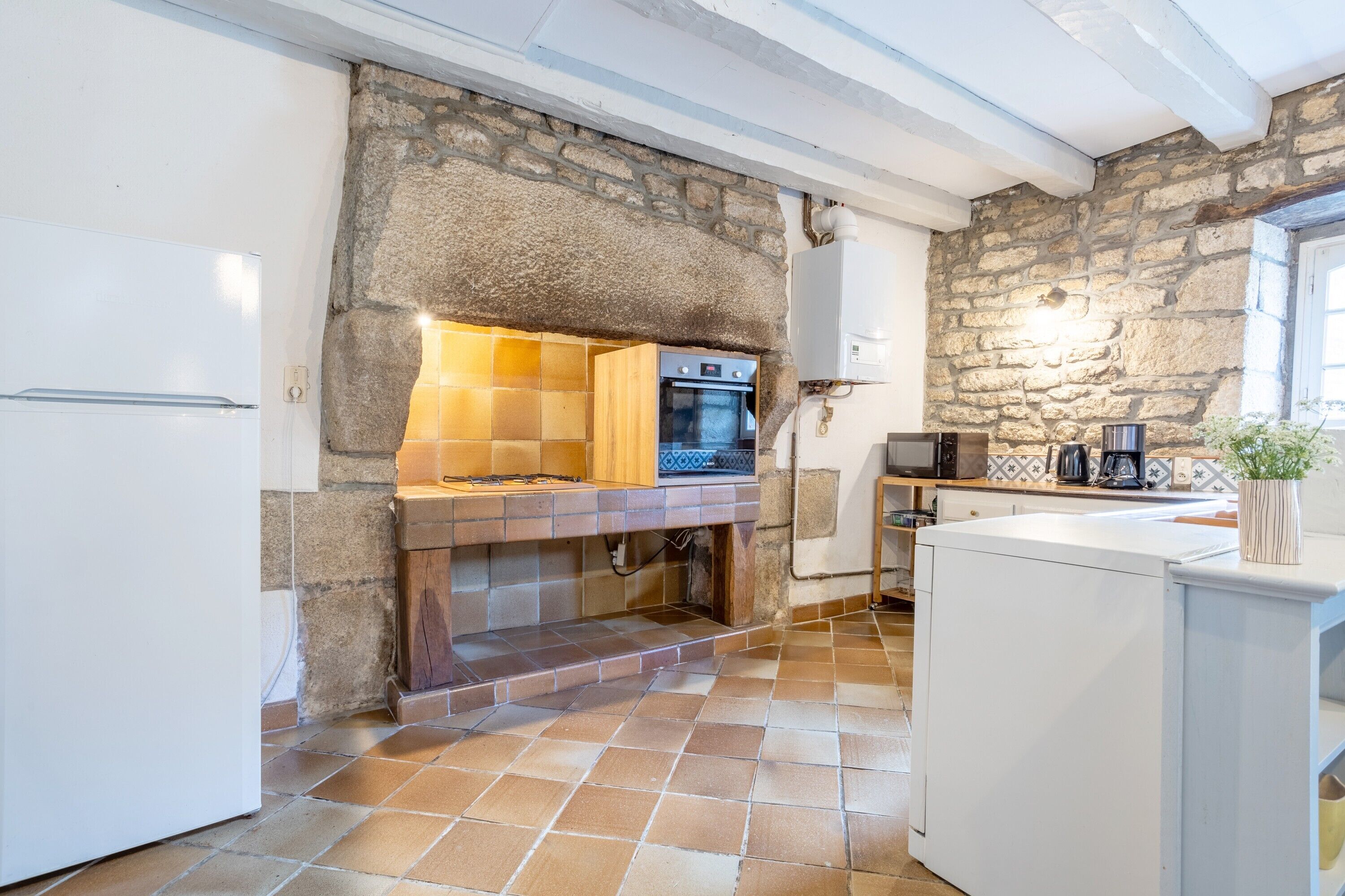Una cocina con pared de piedra, horno empotrado y refrigerador blanco.